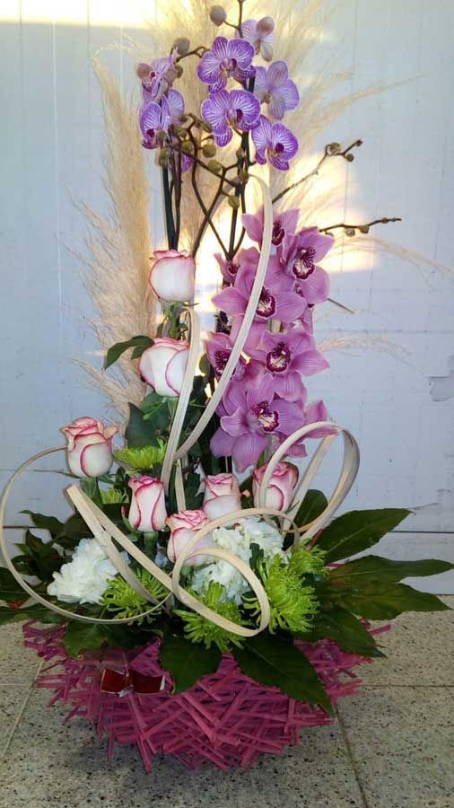Un ramo de orquídeas moradas y rosas blancas en una canasta rosa.