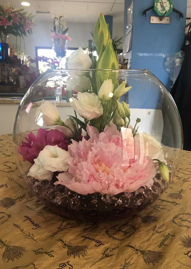 Un cuenco de cristal lleno de flores rosas y blancas sobre una mesa.