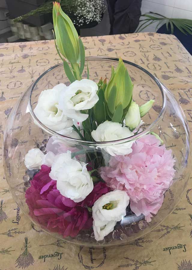 Un cuenco de cristal lleno de flores rosas y blancas sobre una mesa.