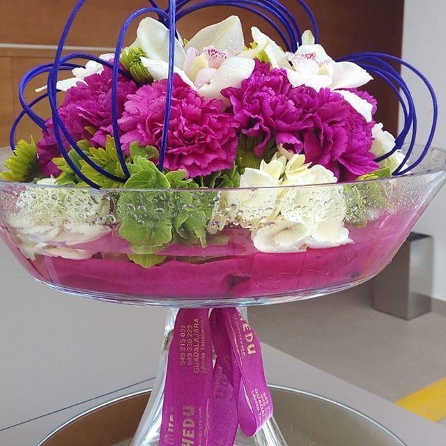 Un jarrón lleno de flores moradas y blancas tiene una cinta que dice vedu.