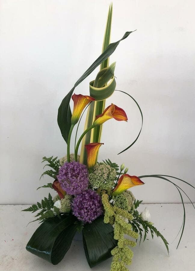 Un jarrón lleno de flores y vegetación sobre una mesa.