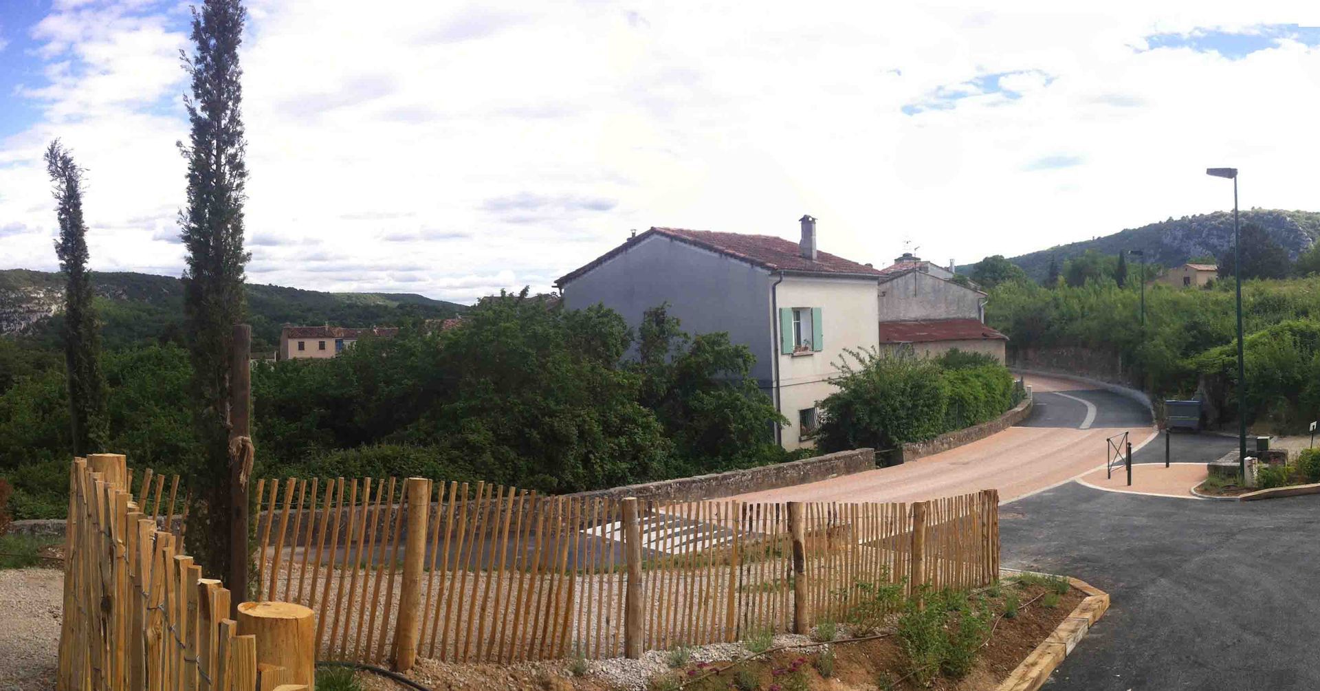 Rue rurale avec des maisons, des arbres et une clôture en bois.