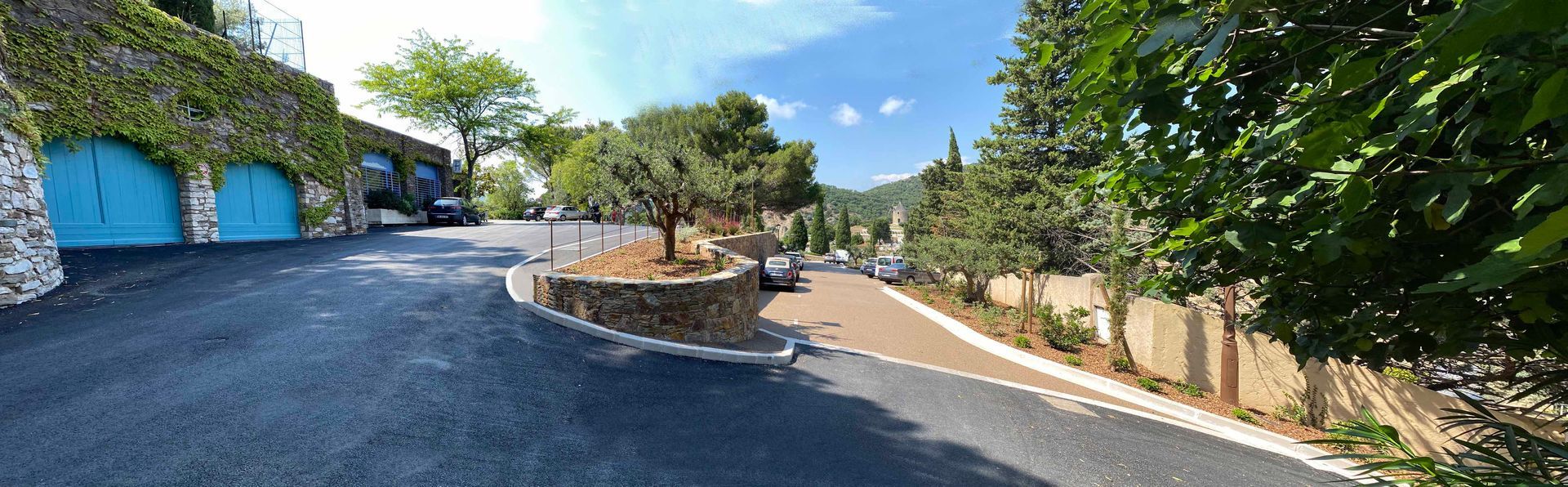 Allée bordant des garages bleus, avec une jardinière ronde et des arbres.