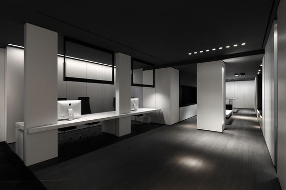 Intérieur de bureau avec bureaux blancs, cloisons et sol foncé, vu depuis un couloir