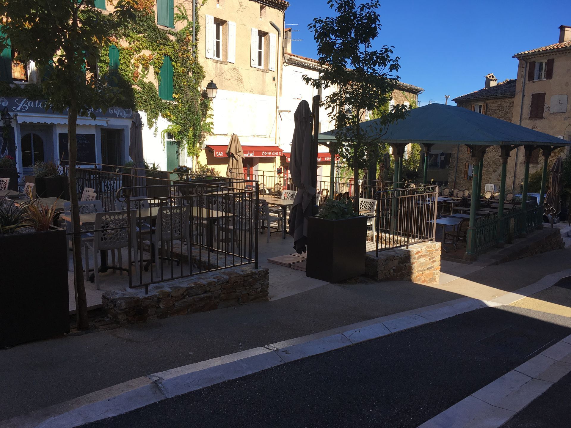 Terrasse d'un café en plein air avec tables, chaises, parasols et bâtiments en pierre en arrière-plan