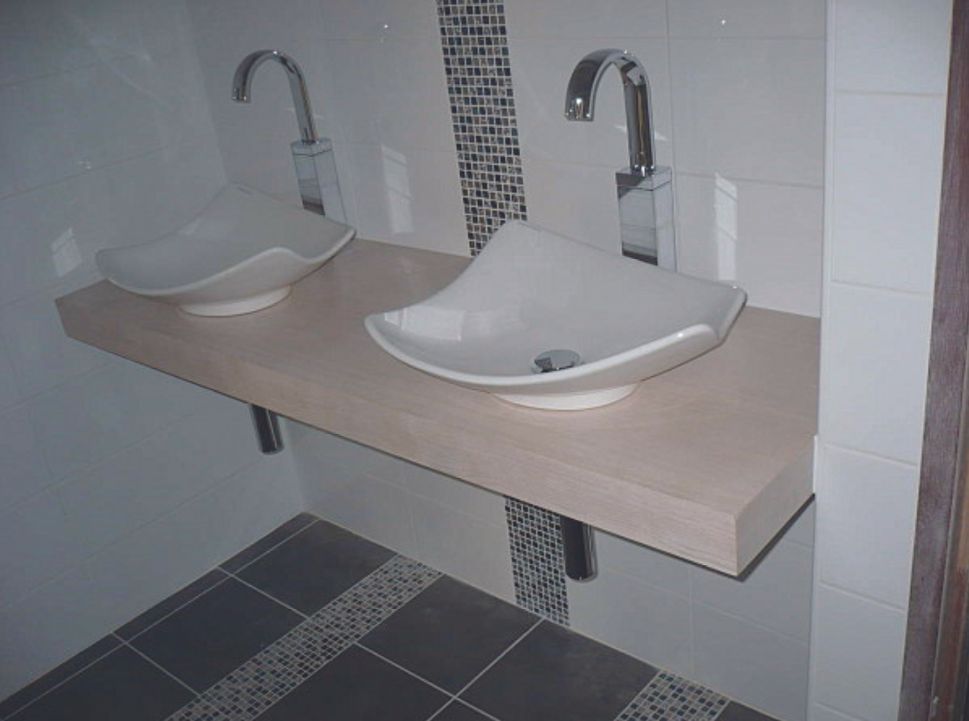Deux lavabos blancs fixés au mur sur un meuble beige dans une salle de bains carrelée