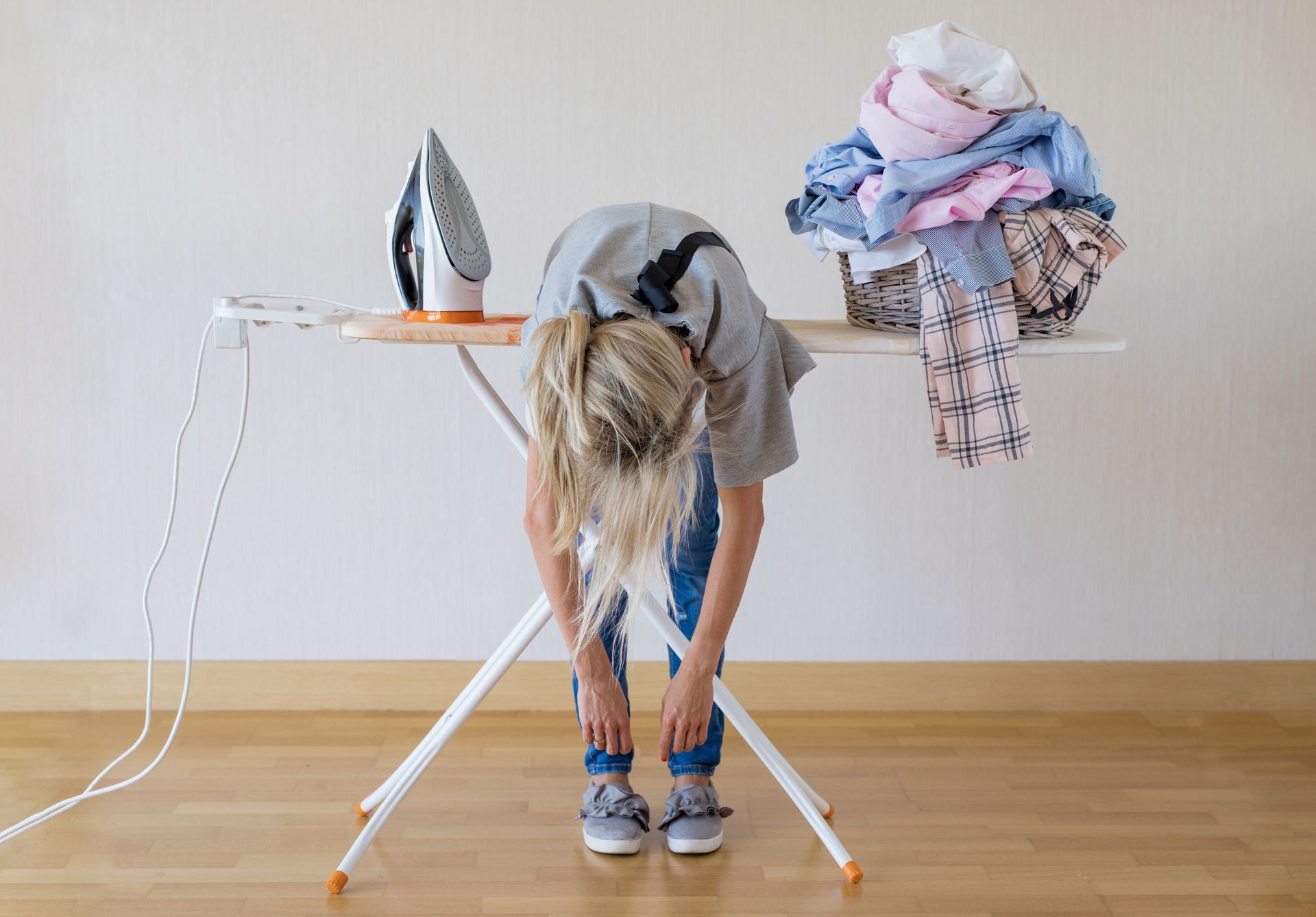 Une femme penchée sur une table à repasser et un tas de linge