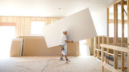 Un hombre lleva un gran trozo de yeso en una habitación en construcción.