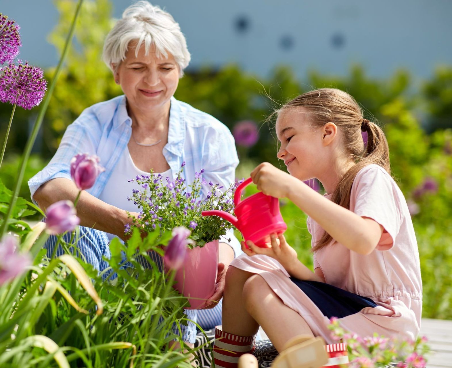 Une petite fille arrose une fleur en pot accompagnée d'une femme plus agée