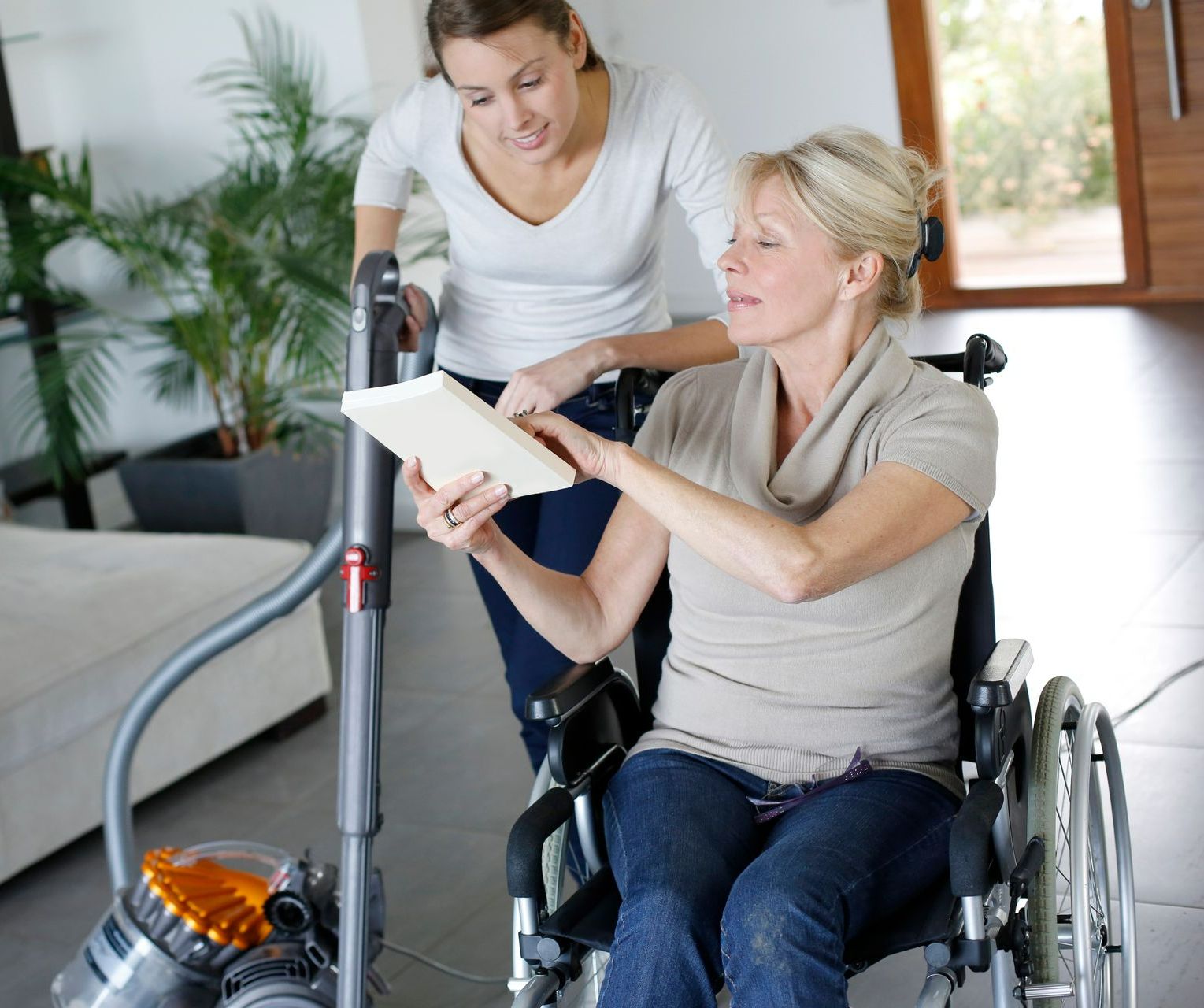 Une assistante passe l'aspirateur avec une personne handicapée