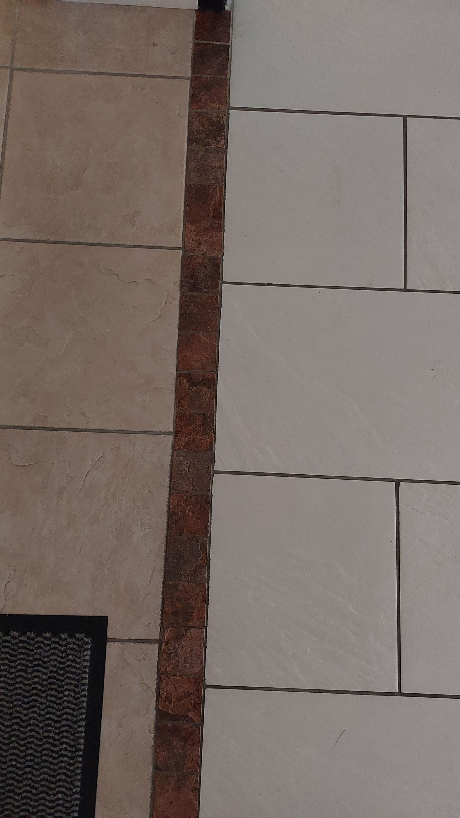 Sol carrelé avec une bordure étroite, façon brique, séparant des carreaux rectangulaires beige et gris clair.