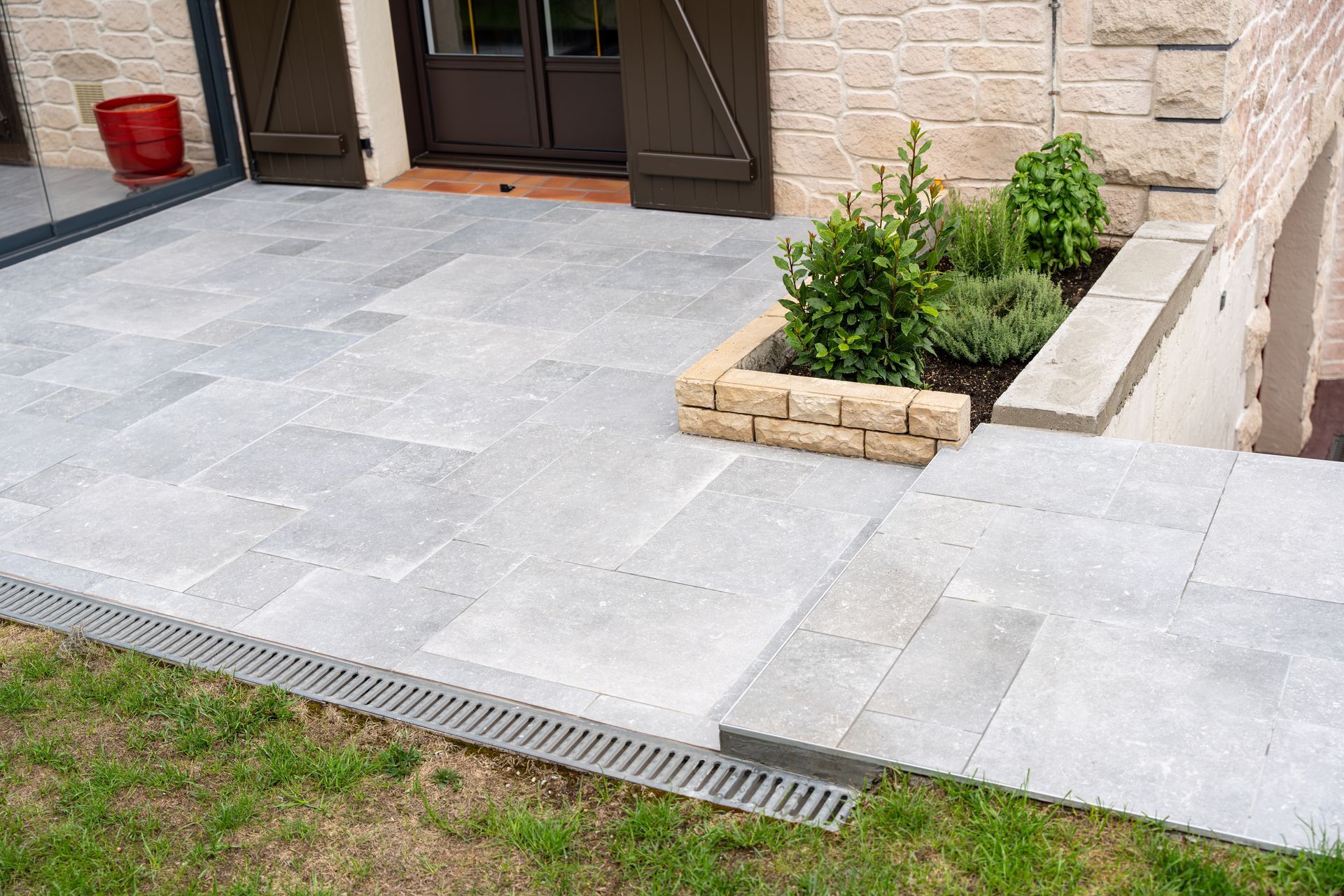Terrasse en pierre avec jardinière intégrée et marches. Un caniveau longe le pourtour, à côté de la pelouse.