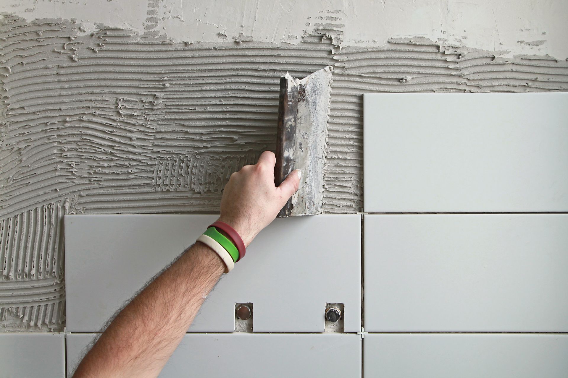 Personne posant du carrelage, utilisant une truelle pour appliquer du mortier sur un mur en vue de la pose de carrelage.
