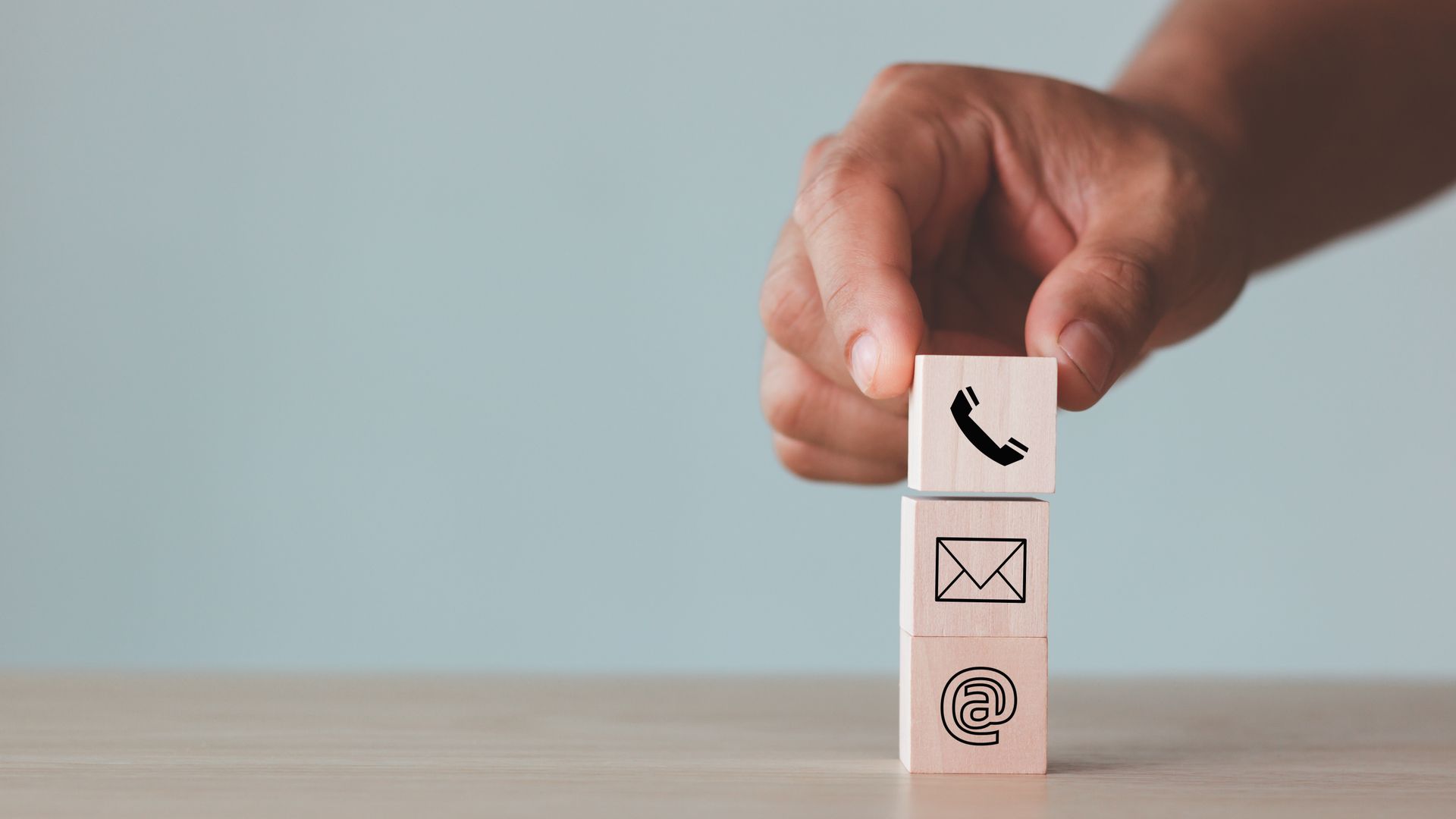 Une main place un bloc de bois orné d'une icône de téléphone sur des blocs portant des icônes d'e-mail et de site web.