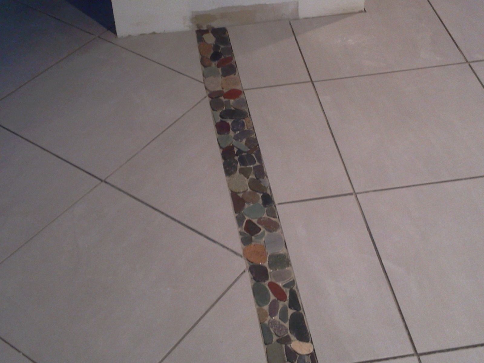 Sol carrelé de carreaux carrés clairs et orné d'une frise décorative de petits cailloux colorés.