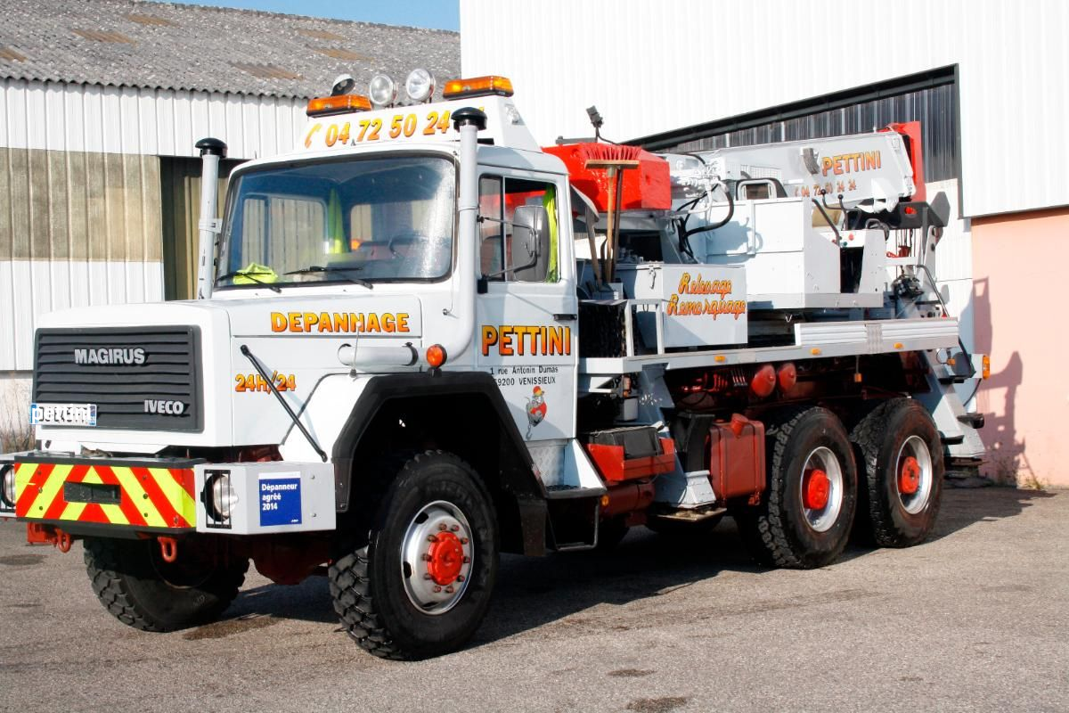 Camion IVECO blanc avec nacelle élévatrice orange, stationné devant un bâtiment.