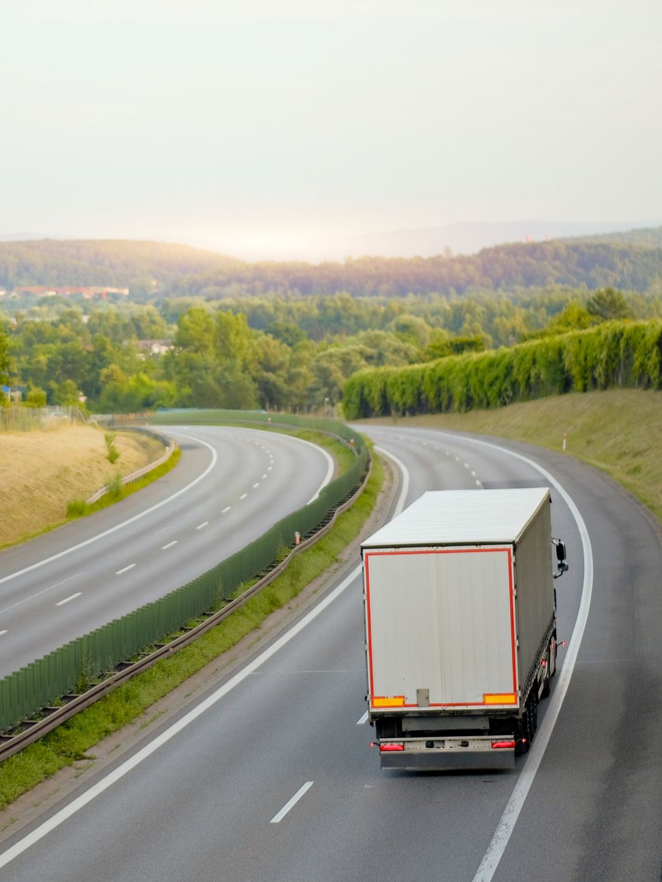 Un semi-remorque sur une route sinueuse, traversant un paysage verdoyant sous un ciel couvert.