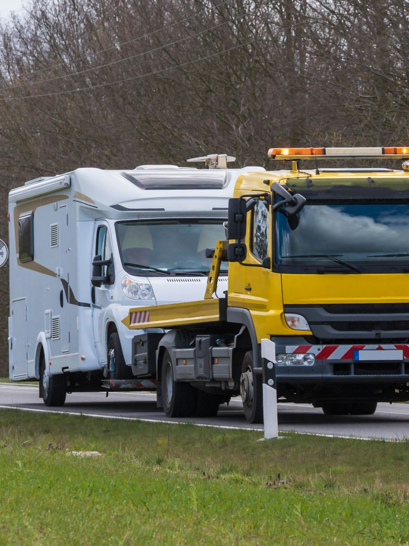 Une dépanneuse jaune remorque un camping-car blanc sur la route.