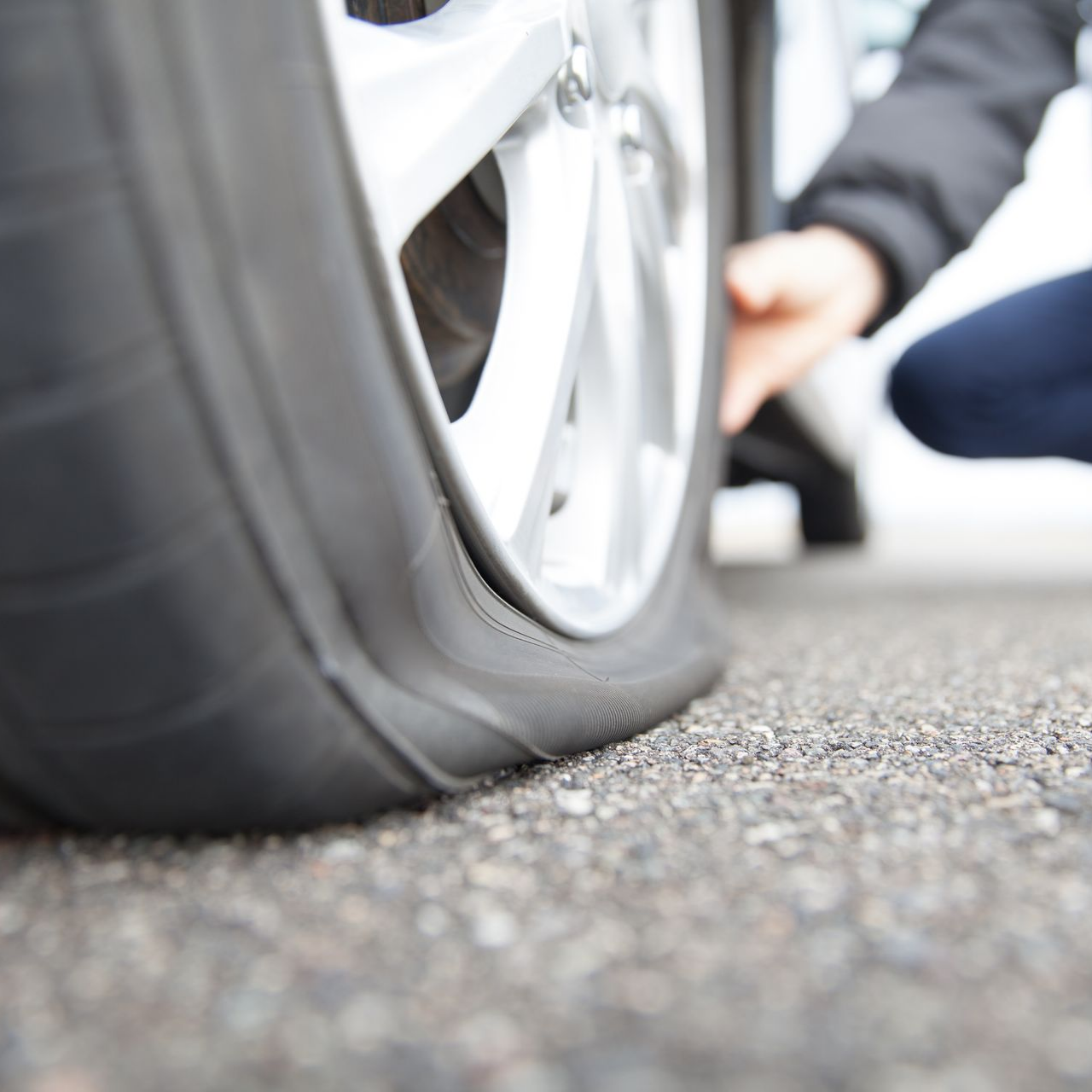 Pneu crevé sur l'asphalte ; une personne vérifie le pneu.