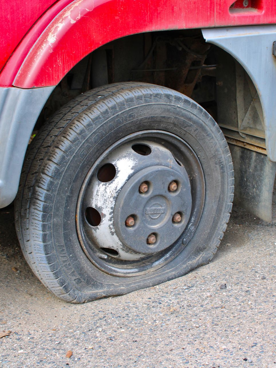 Pneu crevé sur un véhicule rouge ; la roue dégonflée repose sur du gravier.
