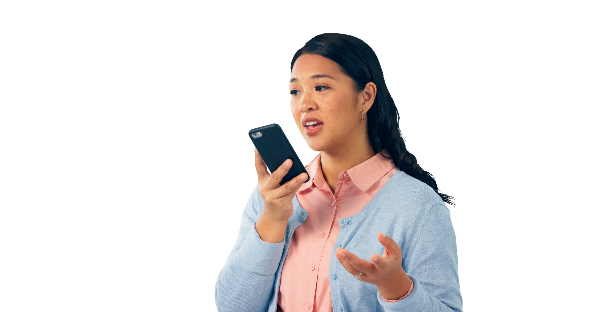 Femme tenant un smartphone, parlant et gesticulant. Elle porte une chemise rose et un cardigan bleu.