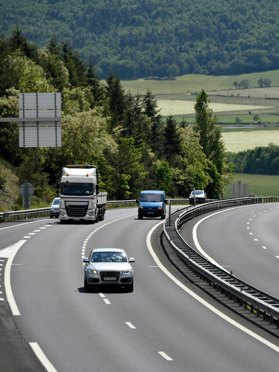 Autoroute avec des véhicules circulant sur une route sinueuse, paysage verdoyant luxuriant en arrière-plan.
