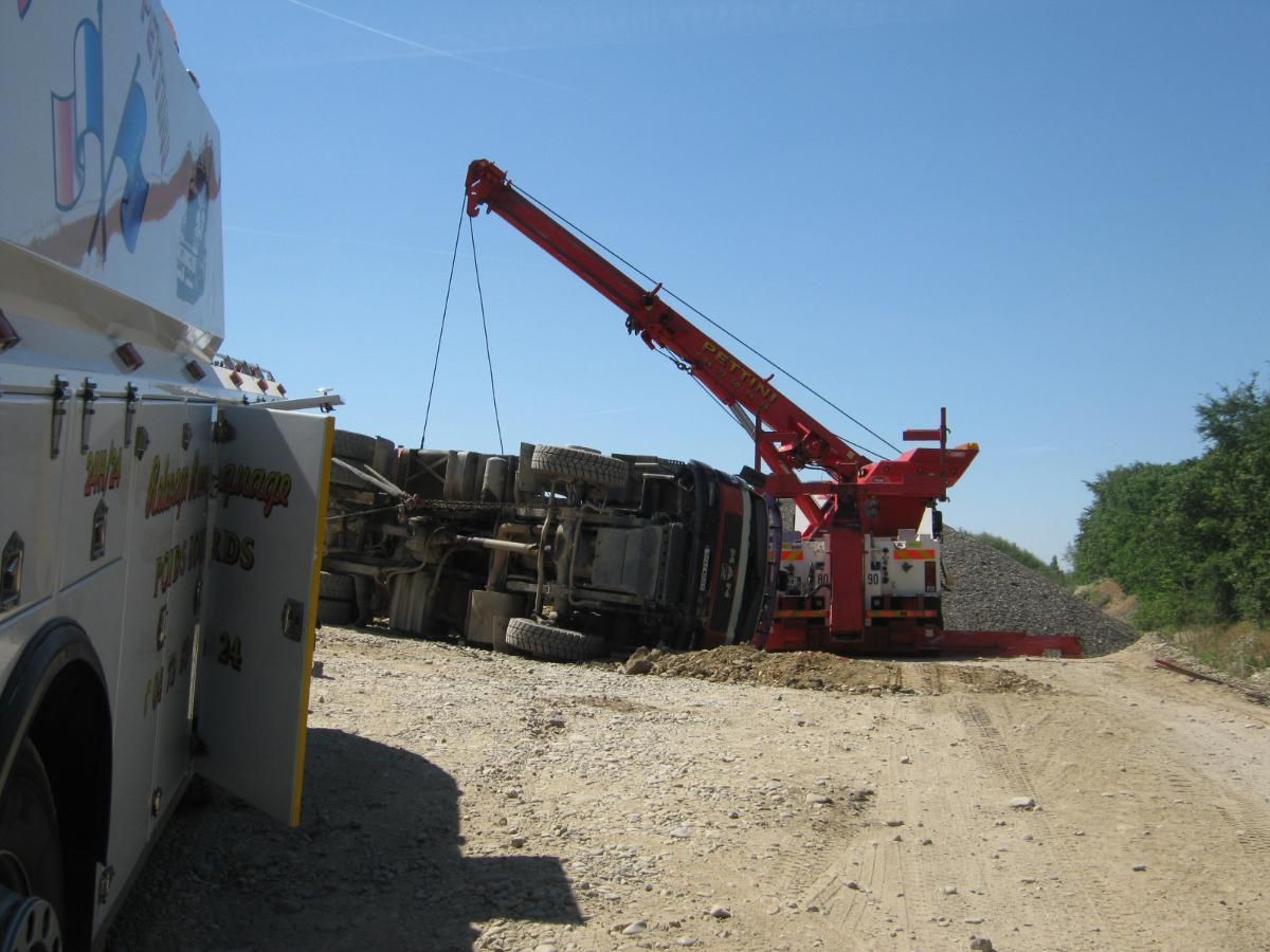 Un semi-remorque s'est renversé sur une autoroute ; le conteneur est couché sur le côté, les roues sont visibles. Une personne se tient à proximité.