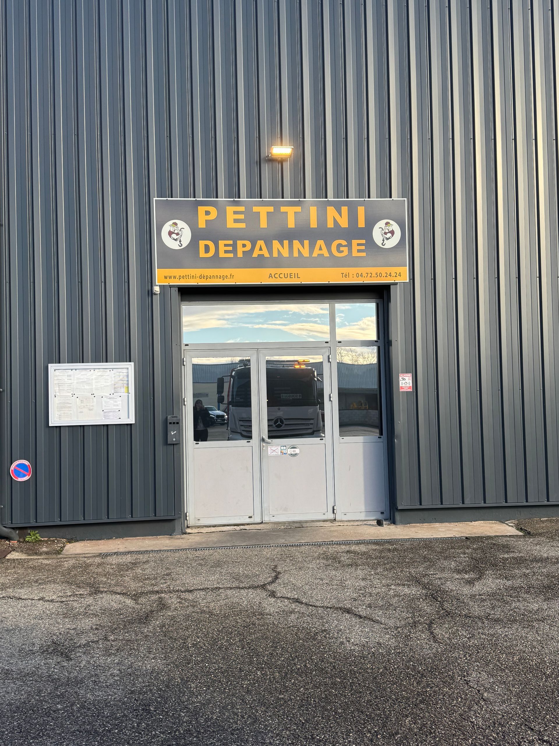 Bâtiment rouge et blanc avec l'enseigne PETTINI DEPANNAGES, portes grises portant l'inscription ACCUEIL.