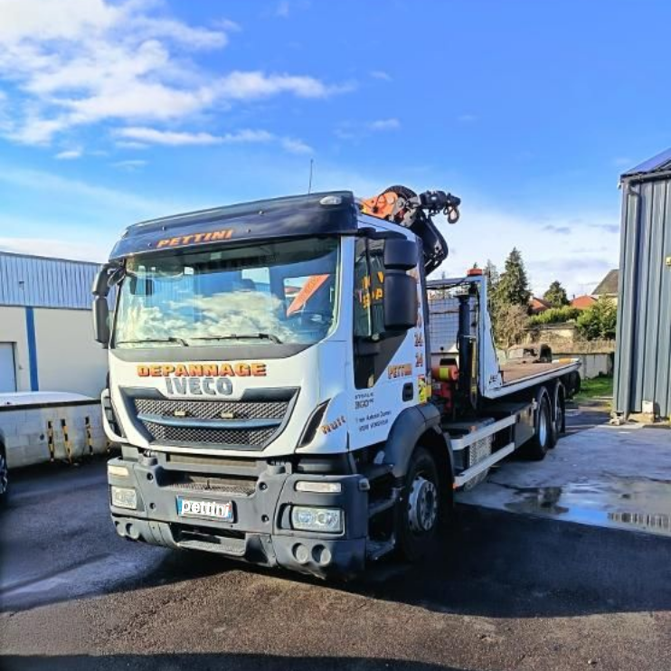 Une dépanneuse rouge sur une route mouillée, flèche déployée. Une personne en veste orange se tient à proximité.