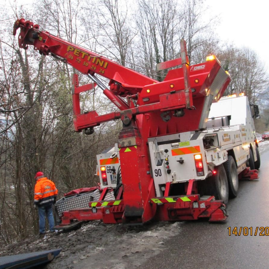Camion de dépannage rouge sur une route boueuse, flèche déployée, opérateur en gilet orange à proximité.
