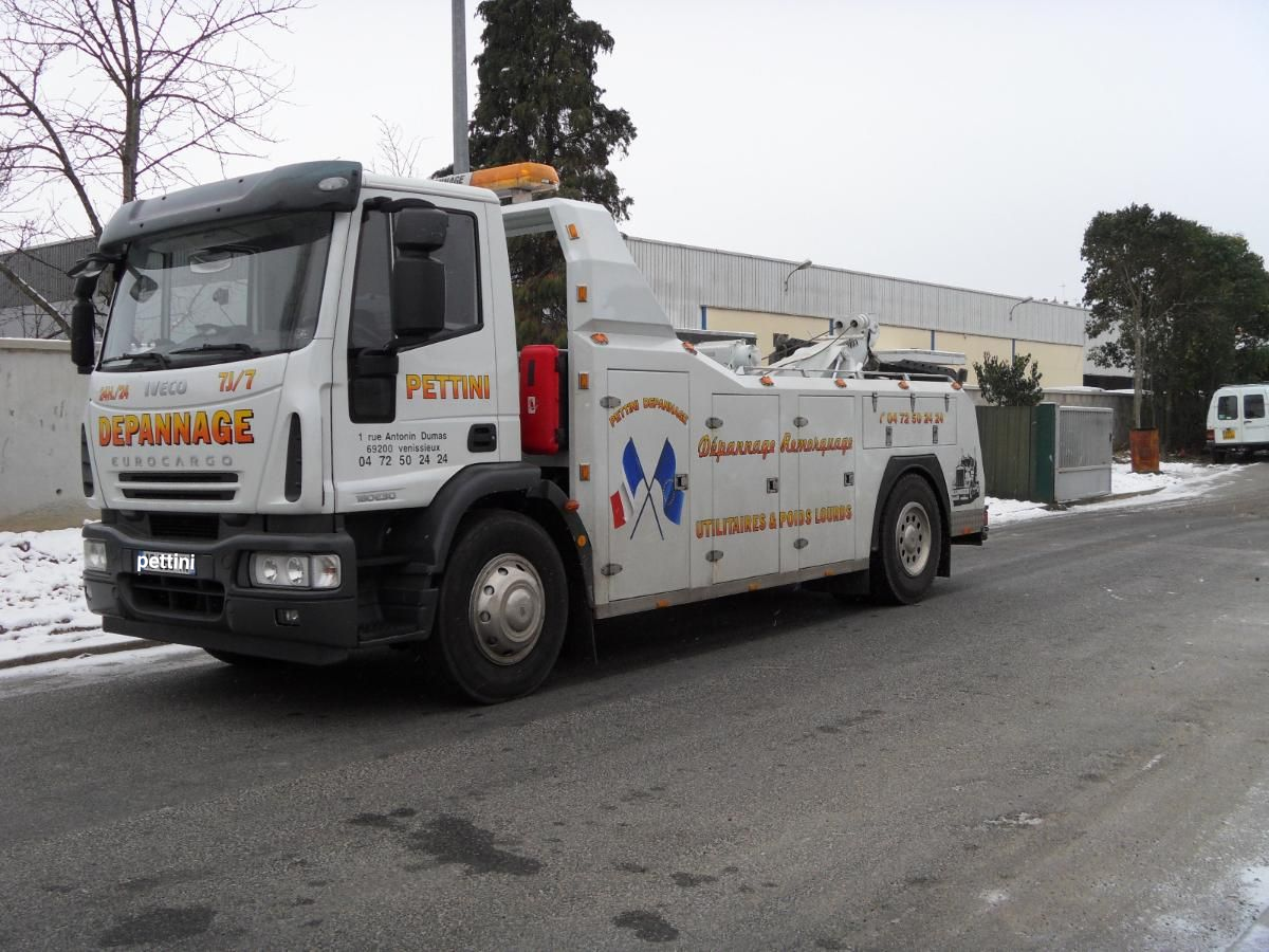 Dépanneuse sur une rue enneigée, camion blanc avec le nom et le logo de l'entreprise, ciel couvert.
