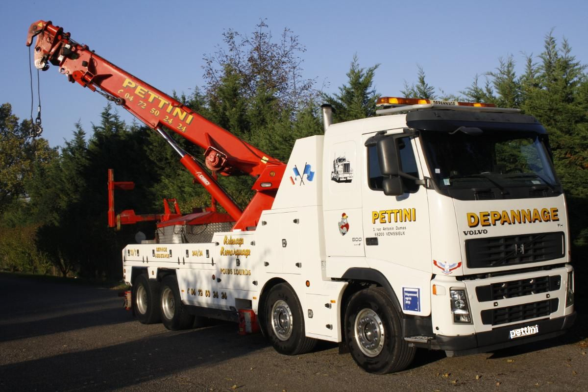 Voiture blanche sur une dépanneuse circulant sur une autoroute. Arbres verts et autres véhicules en arrière-plan.