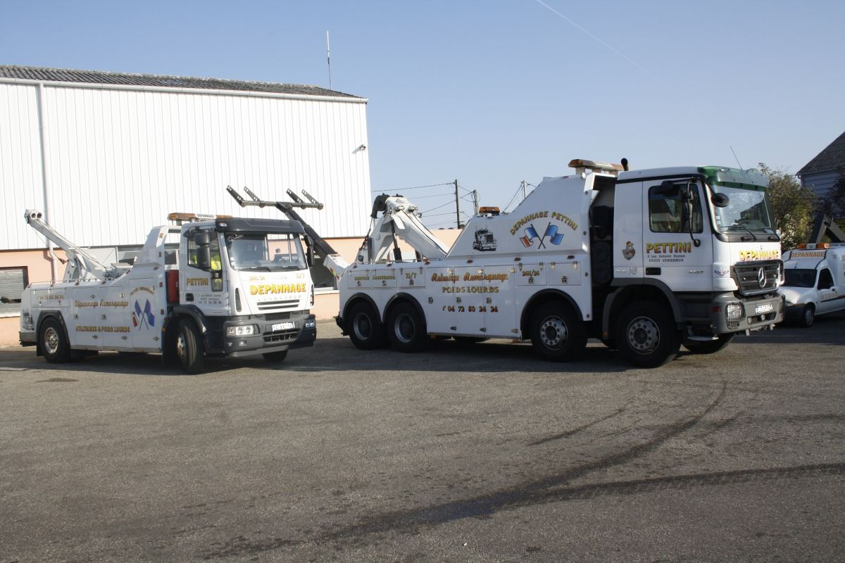 Deux dépanneuses blanches garées devant un bâtiment blanc par une journée ensoleillée.