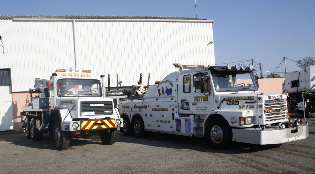 Deux dépanneuses blanches garées devant un bâtiment par une journée ensoleillée.