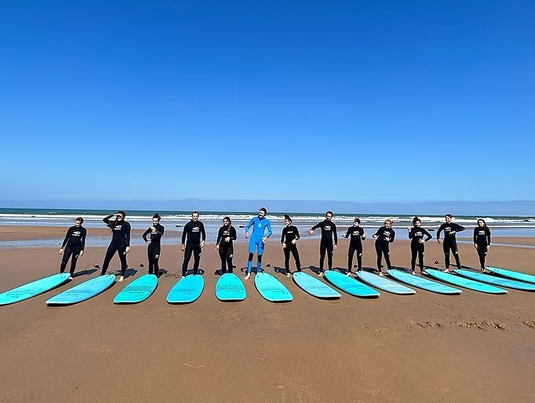 A woman in a swimsuit relaxes on a sunbed by a turquoise pool in a courtyard. White chairs.