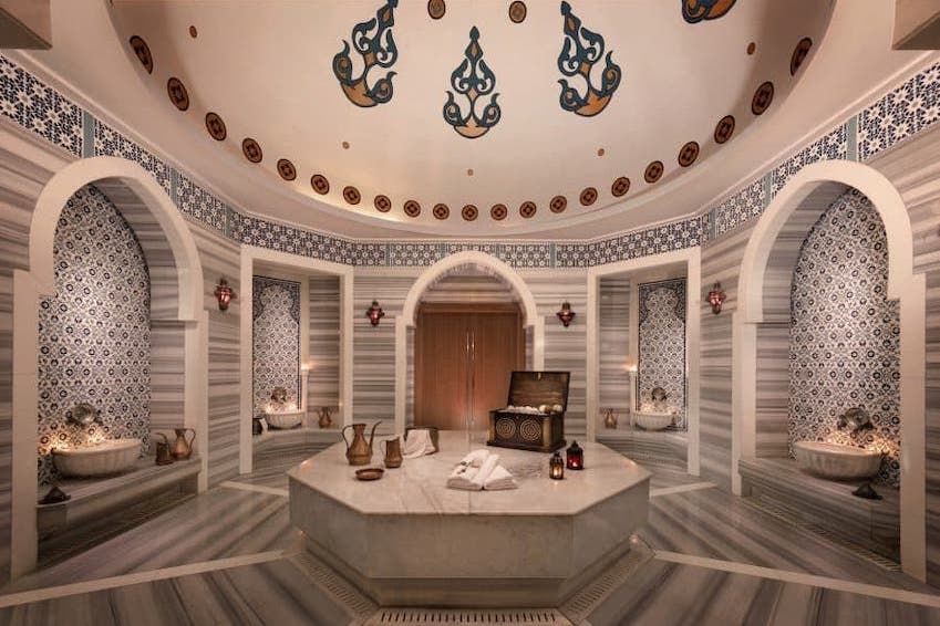 Elegant Moroccan HAMMAM, marble and mosaic tiles, arched doorways, central octagonal table, dome ceiling.