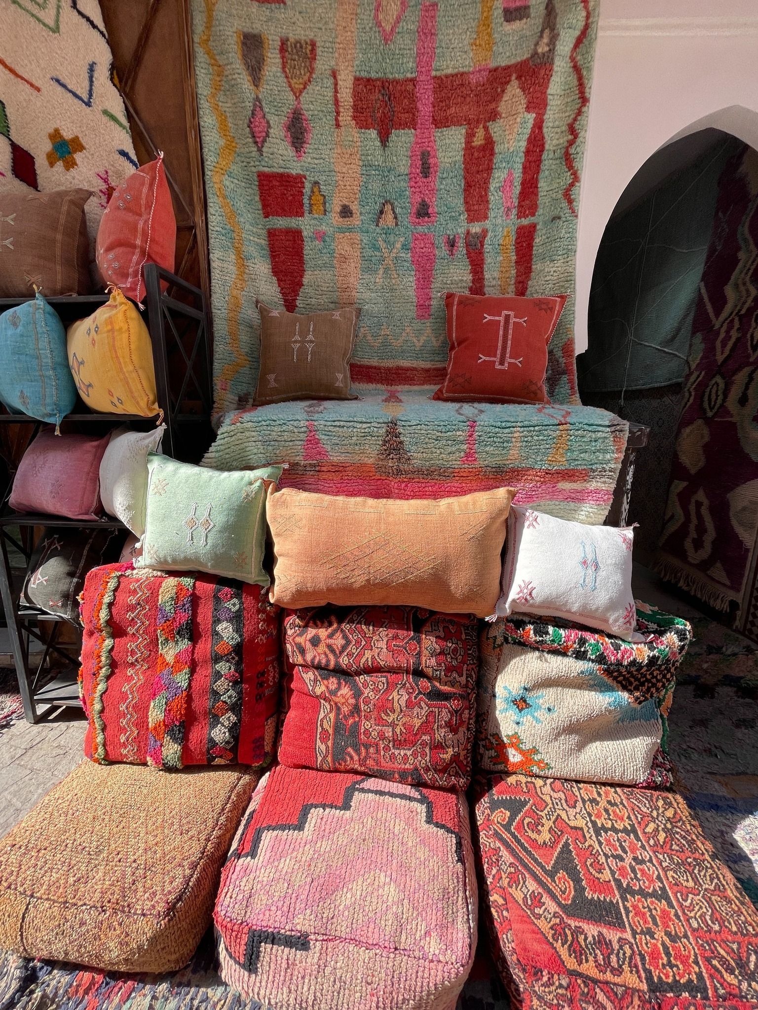 Shop display with colorful pillows and rugs; red, turquoise, and tan hues dominate.