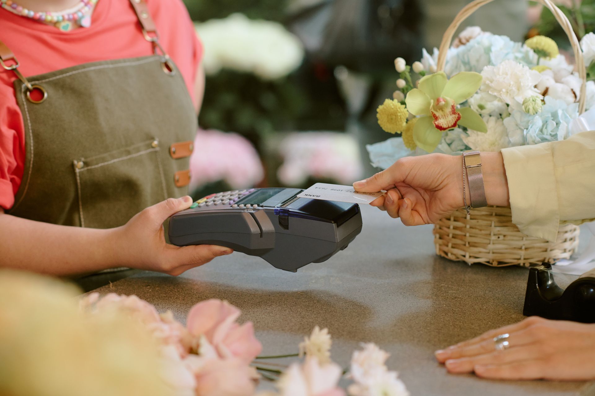 Un vendeur tend un lecteur de cartes à un client au comptoir d'une boutique de fleurs.