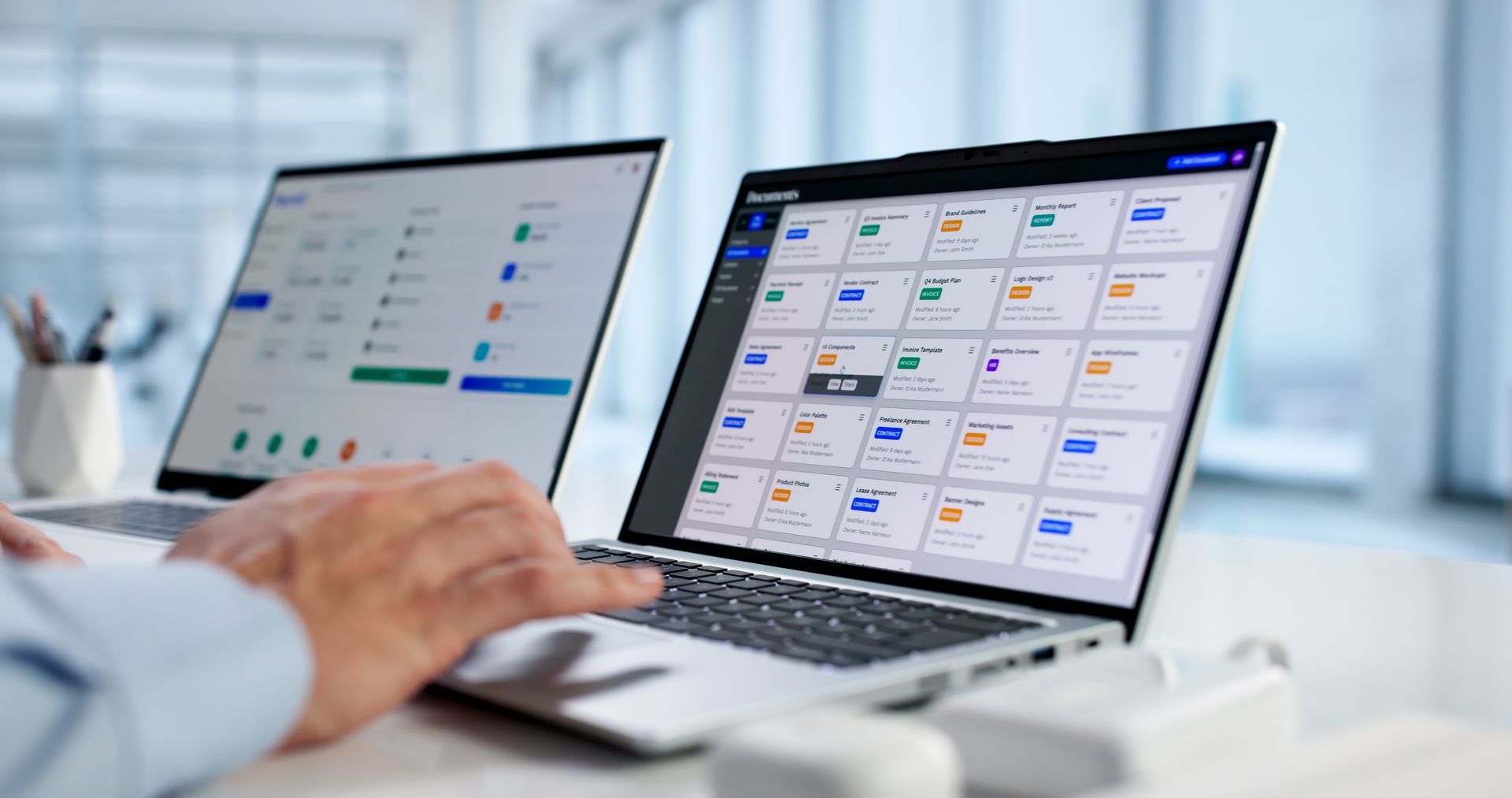 Des mains manipulant un ordinateur portable à côté d'un écran externe affichent toutes deux des tableaux de bord d'applications dans un bureau lumineux.