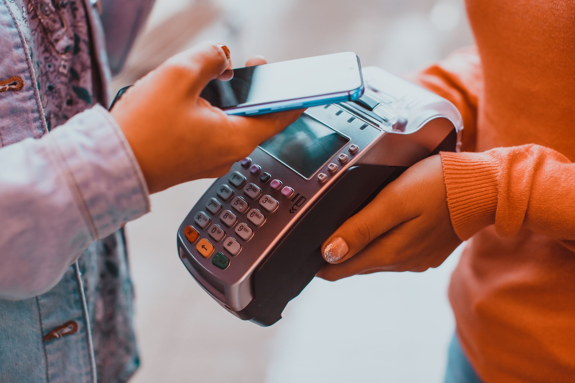Deux personnes utilisent un smartphone pour payer à un terminal de paiement sans contact.