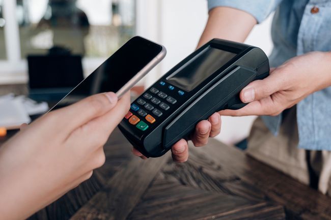 Paiement sans contact à un terminal de carte avec un téléphone et une carte présentés par deux mains.