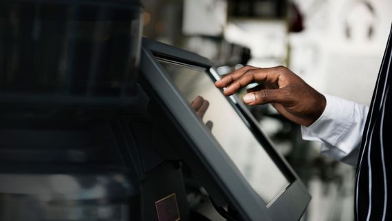 Main appuyant sur un kiosque à écran tactile dans un environnement intérieur moderne.