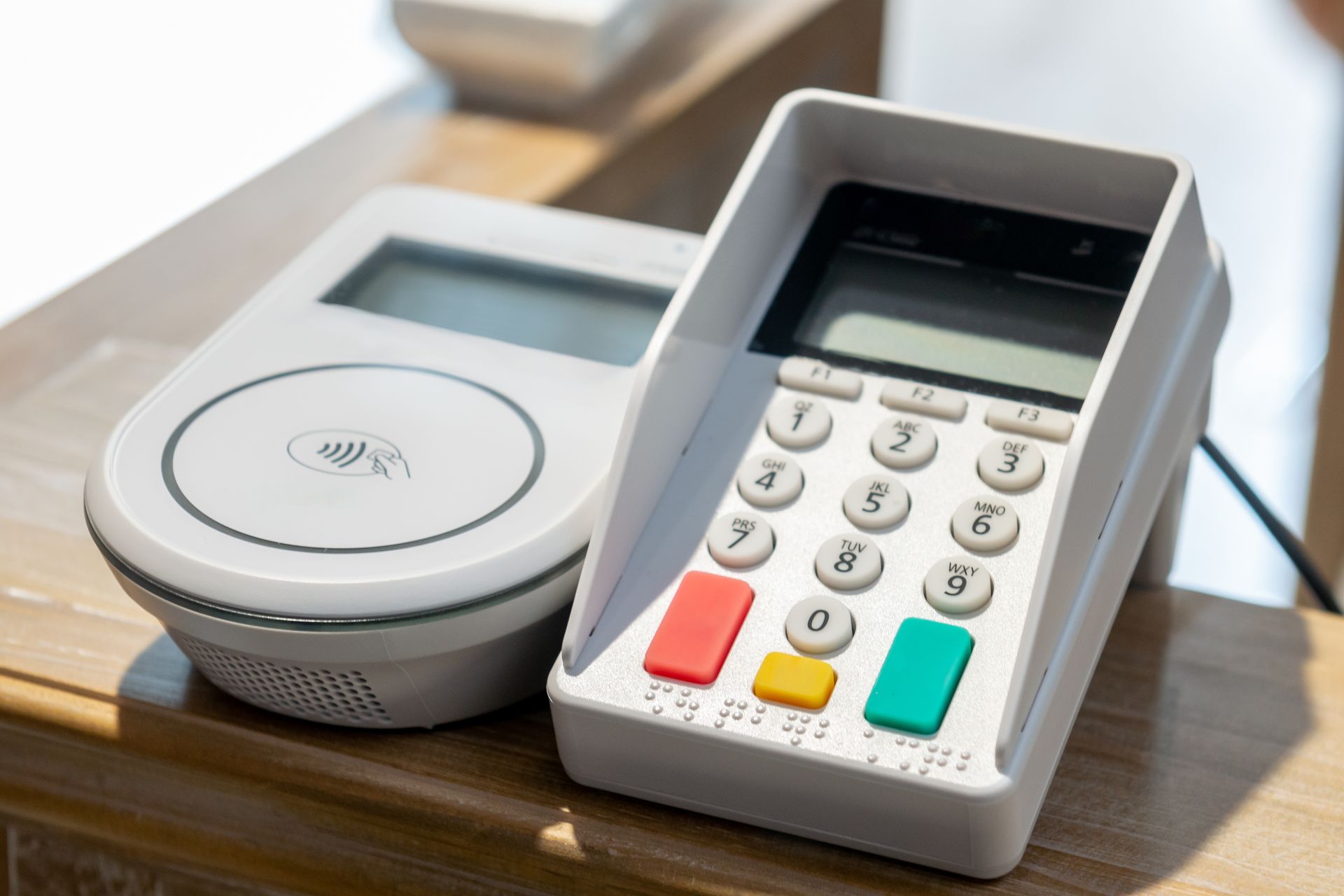 Terminal de paiement sans contact avec clavier et lecteur de cartes sur un comptoir en bois.