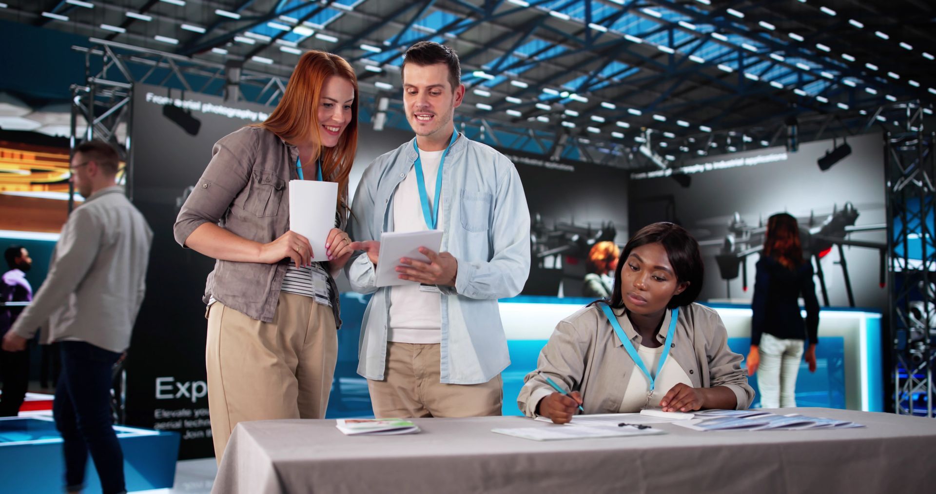 Stand d'exposition avec trois personnes s'inscrivant à une table sous les lumières vives du hall des congrès.
