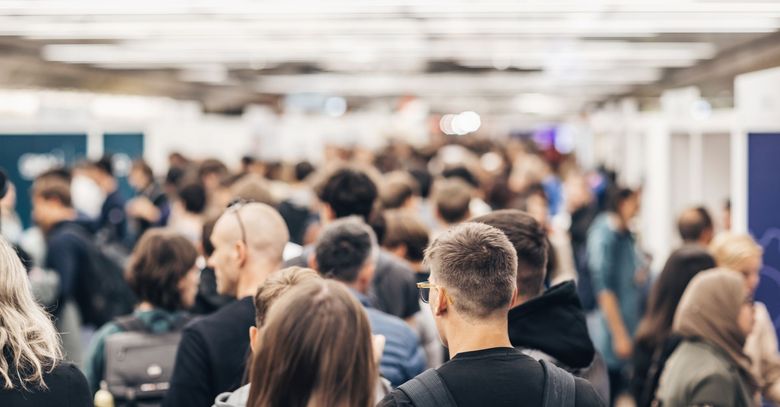 Événement en intérieur bondé, les gens étant vus de dos dans une salle lumineuse et floue.