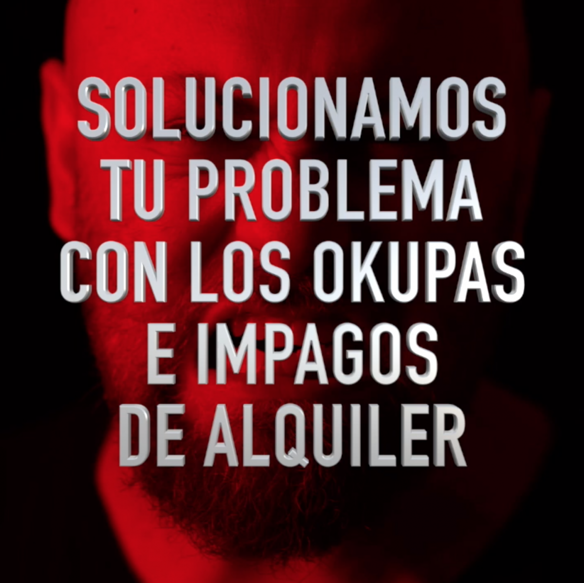 A man with a beard is behind a sign that says solucionamos tu problema con los okupas e impagos de alquiler