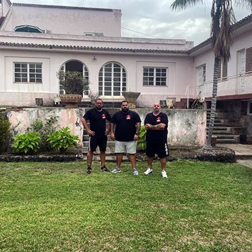 Tres hombres posan para una fotografía frente a una casa.