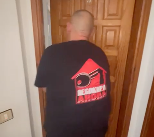 Un hombre que lleva una camisa negra con una casa roja y una llave en ella.