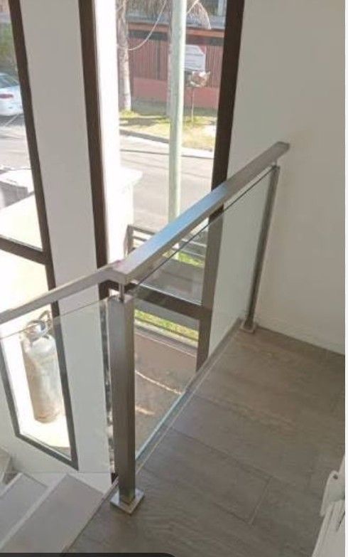 Rellano de escalera con barandilla de cristal junto a grandes ventanales y vistas al exterior.