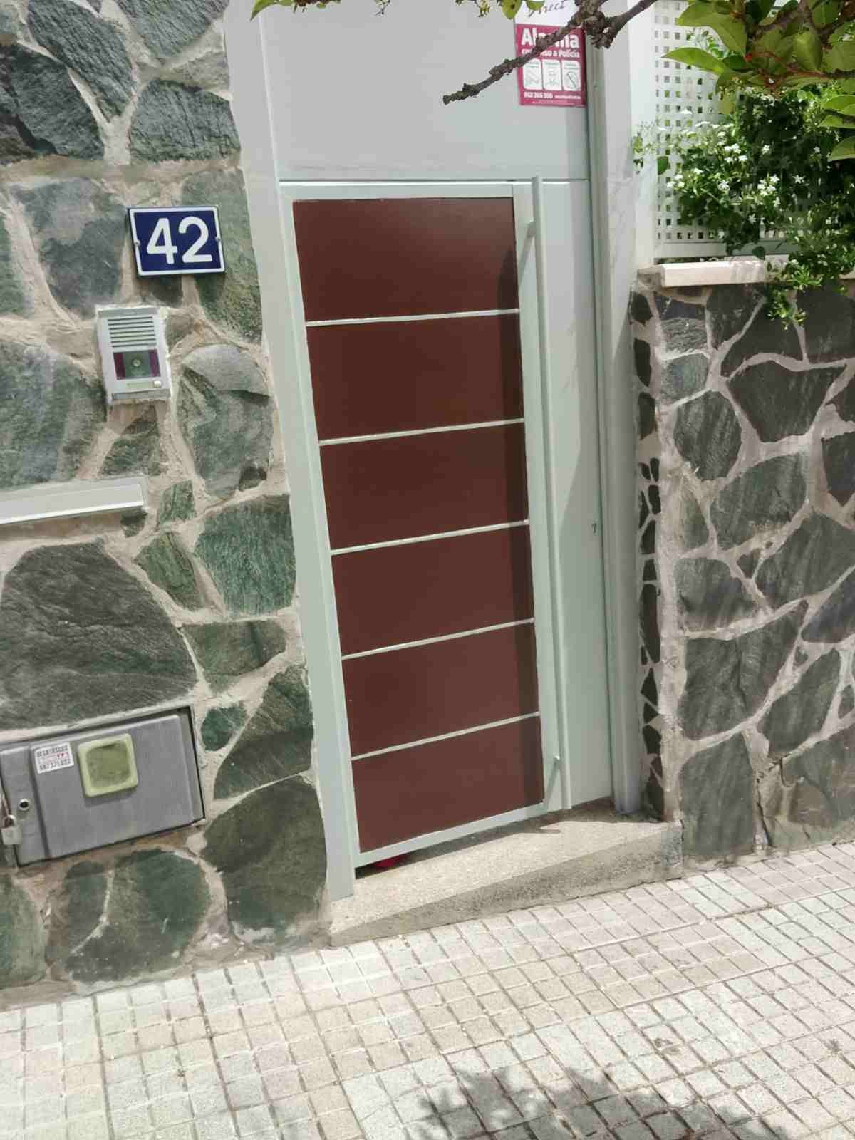 Entrada de la casa con puerta de metal roja, paredes de piedra y el número 42 encima del buzón.